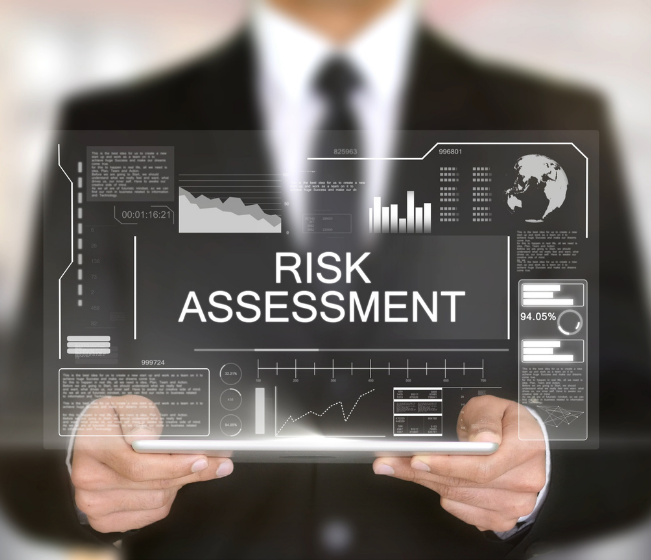 a man in a black suit stands blurred behind a screen which reads "risk assessment" covid-19